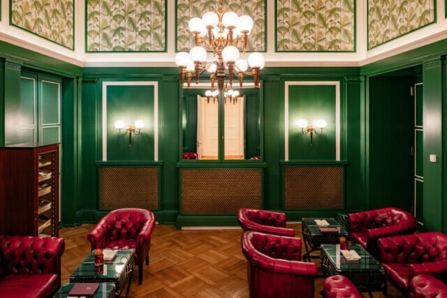 Eleganter Salon mit grünen Wänden, roten Ledersesseln und stilvoller Beleuchtung.