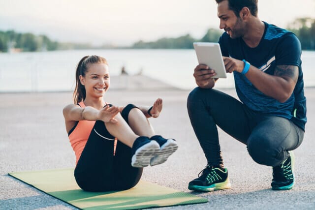 Sportswoman making sit-ups outdoors with the help of a trainer