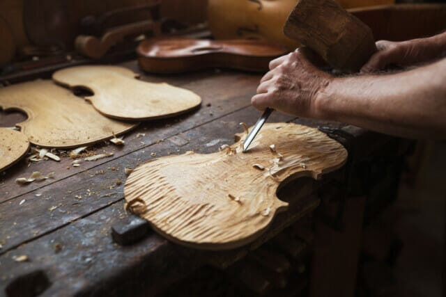Handwerkliche Holzarbeit: Geigenbauer schnitzt eine Holzplatte in der Werkstatt.