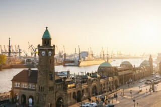 Hafenansicht in Hamburg mit historischen Gebäuden und Kränen im Sonnenuntergang.