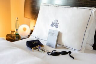 Elegant hotel room with pillow, book, care products and sleep mask on the bed.