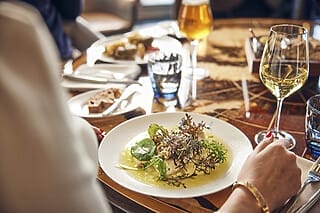Hotel Atlantic Gourmetgericht mit frischen Kräutern, serviert mit Weißwein und Brot auf einem stilvollen Tisch.