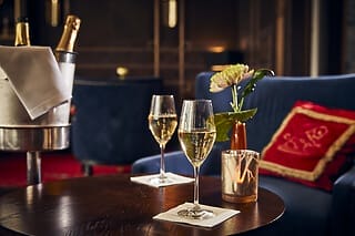 Zwei Gläser Sekt auf einem Tisch neben einer Blume und einem Champagner-Eisbehälter.