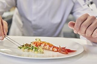 Koch dekoriert einen Teller mit Garnelen und frischen Kräutern in einem eleganten Restaurant.