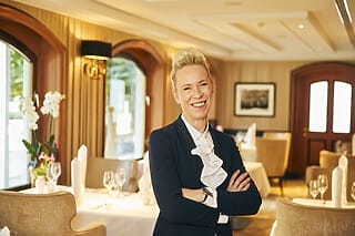 Lächelnde Frau in einem eleganten Restaurant mit gedecktem Tisch und stilvollem Ambiente.